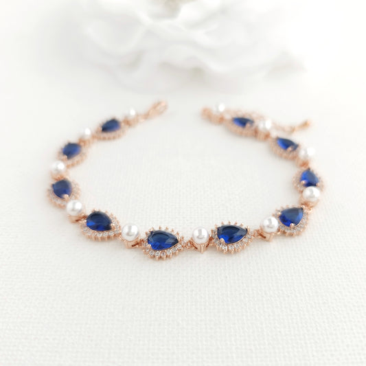 Close-up of elegant rose gold bracelet with blue cubic zirconia crystals and white pearls.