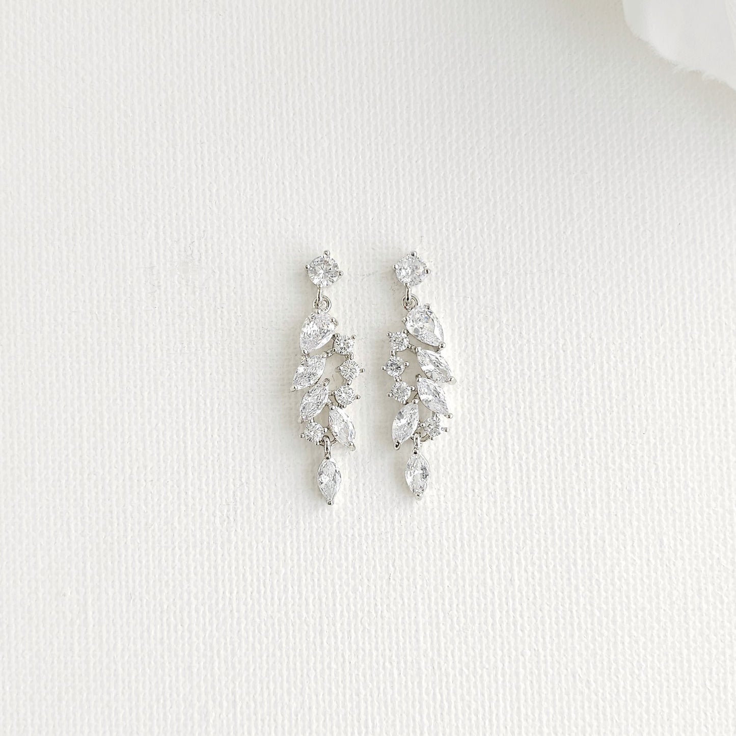 A pair of silver-toned drop earrings with marquise clear stones arranged in a leaf-like cluster, displayed on a textured white surface.