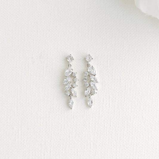 A pair of silver-toned drop earrings with marquise clear stones arranged in a leaf-like cluster, displayed on a textured white surface.